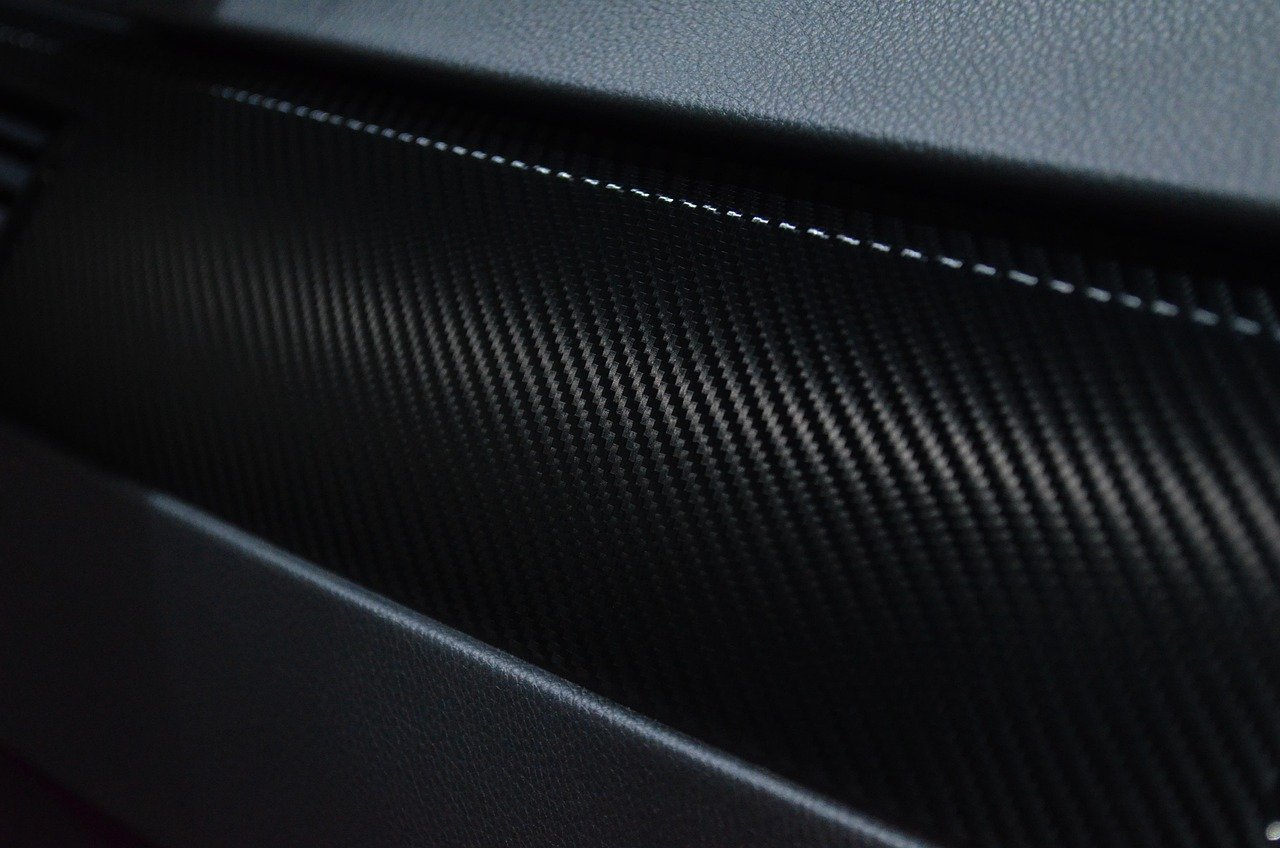 Close-up detail shot of carbon fiber composite material with distinctive diagonal weave pattern and layered texture, showing the technical construction of what appears to be a high-performance component.