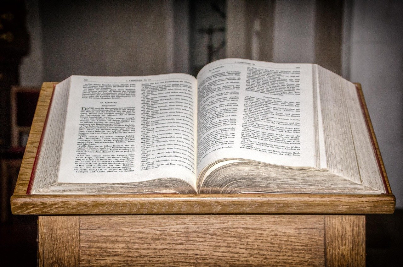 An open book displaying two pages with dense text is positioned on a wooden desk or table surface, photographed from above in natural lighting.