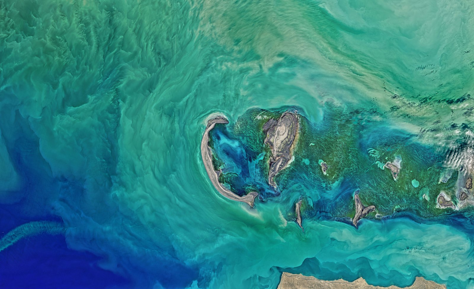 Aerial satellite view of a cluster of small rocky islands surrounded by turquoise and deep blue water, showing natural coastal geography with visible vegetation and geological formations.