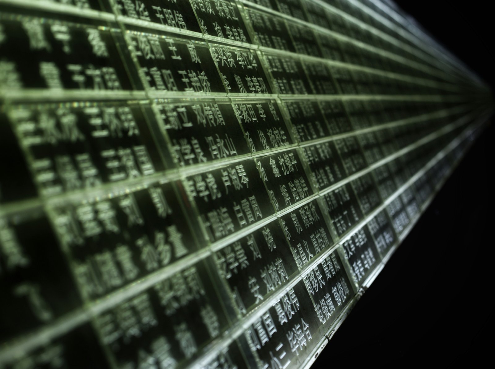 A perspective view of a computer monitor displaying green alphanumeric text and data tables in rows and columns, photographed at an angled depth-of-field perspective suggesting an IT operations or data center environment.