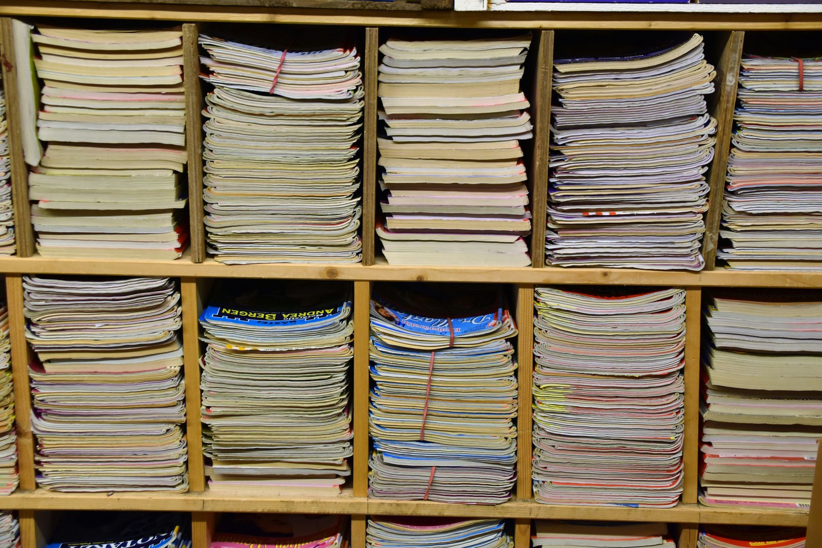Wooden shelving unit filled with neatly stacked papers, documents, and research materials organized in multiple compartments across three rows, with one blue-banded stack visible among predominantly white and colored paper bundles.